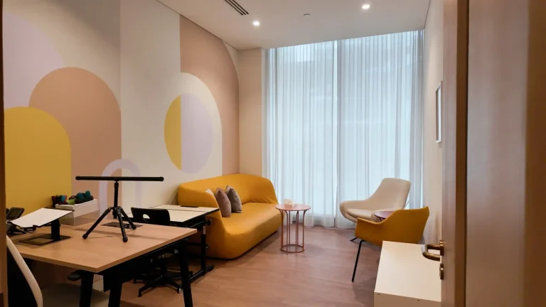 Group therapy room at the alkalma Dubai clinic with a yellow sofa and a pastel arch mural