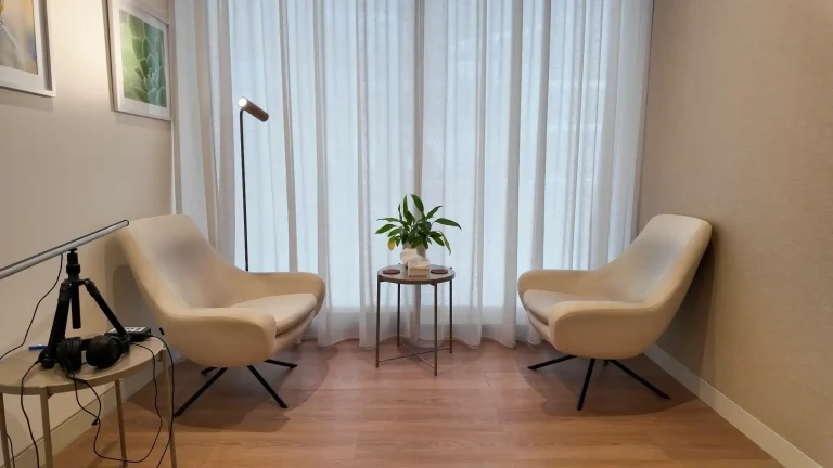 Therapy room at the alkalma Dubai clinic with two armchairs and a small side table beside a curtained window
