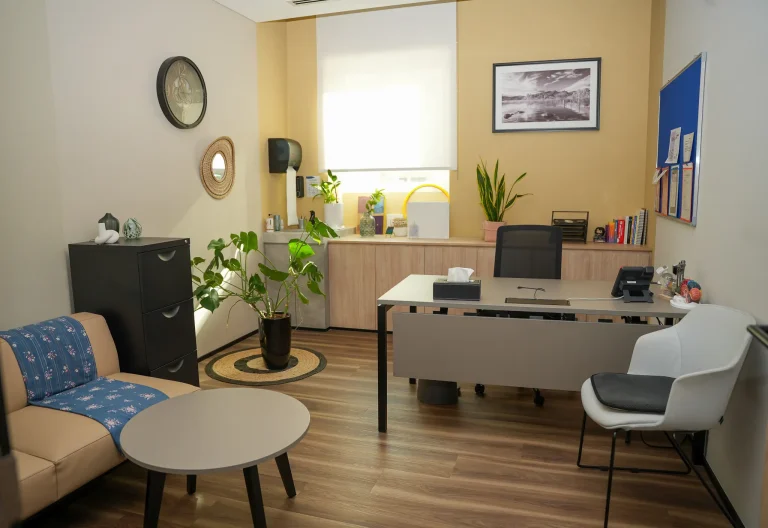 Clinician's office at the alkalma Al Bateen clinic with a desk, bookshelf and indoor plants