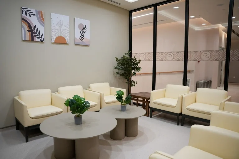 Waiting area at the alkalma Al Falah clinic with cream armchairs, round tables and botanical wall art