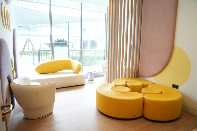 Children's play and waiting area at the alkalma Dubai clinic with curved yellow seating and a garden view