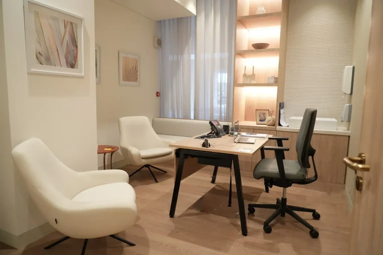 Consultation room at the alkalma Dubai clinic with a desk, two armchairs and warm timber shelving